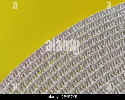 Strohhut auf gelbem Hintergrund. Der Rand des breiten Schirms des Hutes. Fäden oder Zweige binden. Nahaufnahme. Sommerferien-Thema Stockfoto