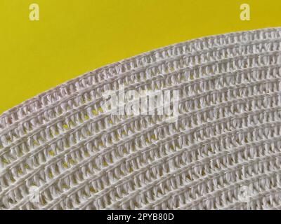 Strohhut auf gelbem Hintergrund. Der Rand des breiten Schirms des Hutes. Fäden oder Zweige binden. Nahaufnahme. Sommerferien-Thema Stockfoto