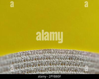 Strohhut auf gelbem Hintergrund. Der Rand des breiten Schirms des Hutes. Fäden oder Zweige binden. Nahaufnahme. Sommerferien-Thema Stockfoto