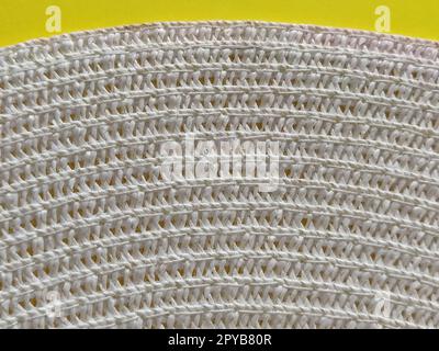 Strohhut auf gelbem Hintergrund. Der Rand des breiten Schirms des Hutes. Fäden oder Zweige binden. Nahaufnahme. Sommerferien-Thema Stockfoto