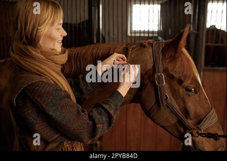 Porträt einer Frau, die im Stall des Reitclubs Pferdemähne flechtet Stockfoto