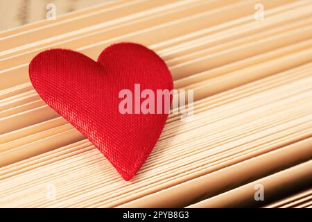 Nahaufnahme des roten Herzens auf dem Hintergrund der Buchseiten Stockfoto