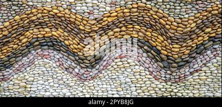 Hintergrund der Wandstruktur aus Kieselstein. Kieselsteinmosaik. Strandkiesel mit Wellenmuster auf Betonwänden abstrakter Hintergrund. Einbettung einzelner Steine in Zement. Natursteinkiesel. Einfache Wand Stockfoto