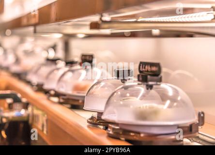 Close-up auf japanischen Förderband Sushi Restaurant, wo sie die Teller mit Sushi auf einer rotierenden Schiene mit einem durchsichtigen Deckel geschützt platziert sind. Stockfoto