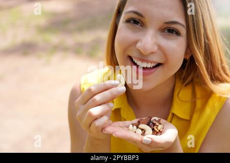 Nahaufnahme eines lächelnden Mädchens, das eine Mischung aus getrockneten Früchten isst und in die Kamera schaut Stockfoto