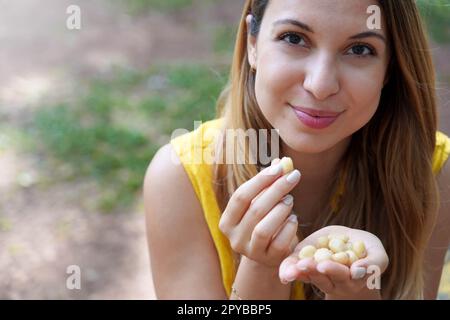 Ein gesundes Mädchen pflückt sich im Park Macadamianüsse aus der Hand. Schaut in die Kamera. Stockfoto