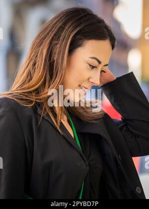 Straßenporträt einer langhaarigen brünetten stehenden asiatischen Rasse, weibliches Model, das aufmerksam aussieht Stockfoto