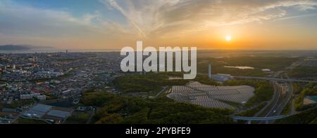 Die Sonne geht auf Sonnenkollektoren in einem kleinen Energiewerk am Rande einer weitläufigen Stadt unter Stockfoto