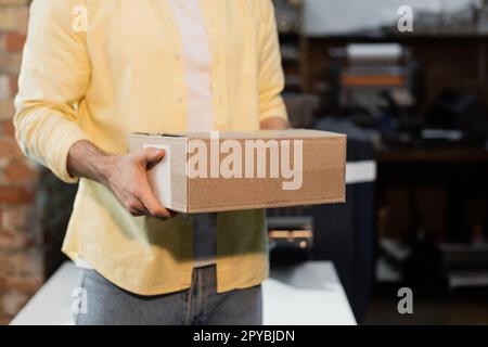 Zugeschnittene Ansicht des Herausgebers, der den Karton im Print Center hält, Aktienbild Stockfoto