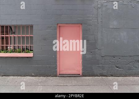 Pinke Tür in einer grauen Backsteinmauer mit einem Fenster in Downtown Seattle, Washington Stockfoto