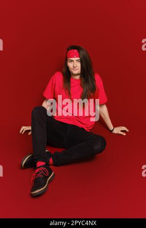Ein Mann mit langen Haaren sitzt auf dem Boden im roten Studio Stockfoto