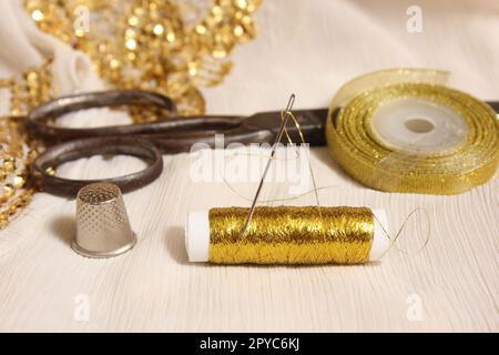 Rolle mit goldenem Gewinde und Schere mit Kaugummi auf weißem Stoff mit goldenen Pailletten Stockfoto