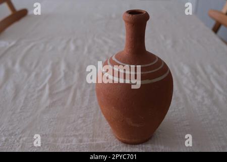 Nahaufnahme eines alten, unlackierten antiken Keramikkastens auf einer weißen Tischdecke. Tonkrug zum Trinken von Wein oder Wasser. Stockfoto