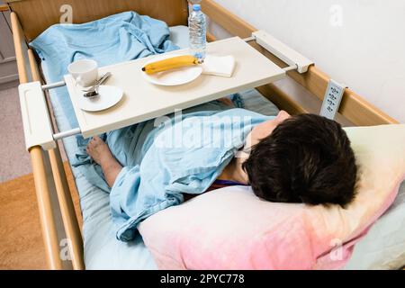 Frau und Tisch mit Geschirr auf dem Krankenhausbett Stockfoto