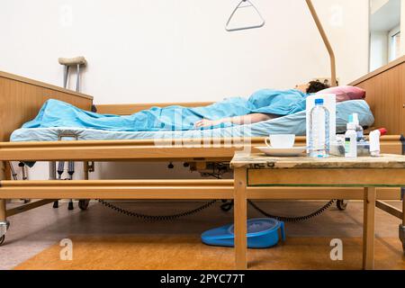 Krankenhausbett mit Kranker und Tisch zu Hause Stockfoto