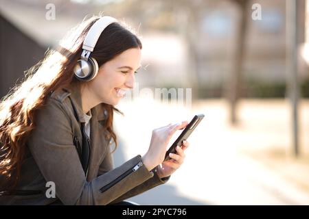 Glückliche Frau, die in einem Park am Telefon Audio hört Stockfoto