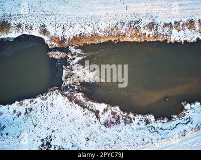 Wasserfall auf dem Winterbach. Schnee an gefrorenen Flussufern. Blick Aus Der Vogelperspektive Auf Den Fluss Cascade. Wasserströmung zwischen Felsen Stockfoto