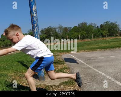 Sremska Mitrovica, Serbien. 6. Juni 2020. Ein Junge spielt Ball auf dem Spielplatz. Asphaltsportplatz. Ein Kind in einem weißen T-Shirt. Kleinkind mit blondem Haar, 7 Jahre alt. Laufen, Treten und Übungen Stockfoto