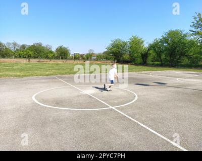 Sremska Mitrovica, Serbien. 6. Juni 2020. Ein Junge spielt Ball auf dem Spielplatz. Asphaltsportplatz. Ein Kind in einem weißen T-Shirt. Kleinkind mit blondem Haar, 7 Jahre alt. Laufen, Treten und Übungen Stockfoto