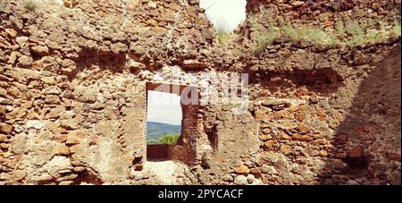 Ruinen einer alten Festung in Vrdnik, Sremska Mitrovica, Vojvodina, Serbien. Alte Steinmauern mit Bergketten im Hintergrund. Touristenattraktionen. Embrasur oder Fenster zur Beobachtung und Verteidigung Stockfoto