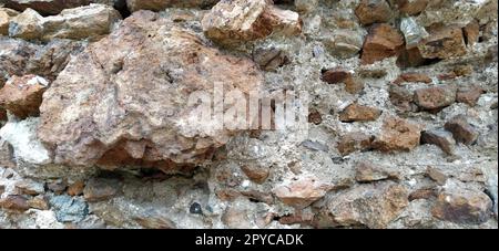 Steinmauer. Gestapelte große Ziegel und Kopfsteinpflaster in warmen Farben. Lose weiße Steine, die aus der Wandoberfläche hervorstehen. Stockfoto