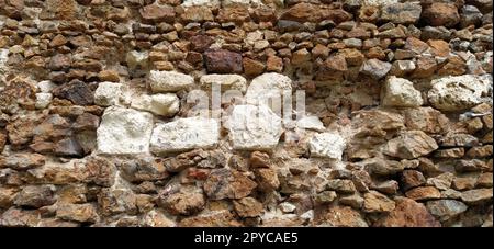 Steinmauer. Gestapelte große Ziegel und Kopfsteinpflaster in warmen Farben. Lose weiße Steine, die aus der Wandoberfläche hervorstehen. Turm in Vrdnik, Serbien. Stockfoto