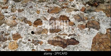 Steinmauer. Gestapelte große Ziegel und Kopfsteinpflaster in warmen Farben. Lose weiße Steine, die aus der Wandoberfläche hervorstehen. Stockfoto