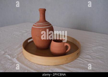 Vorderansicht eines alten unlackierten antiken Keramikkastens in einem Tablett auf einer traditionellen Tischdecke. Clay Utensilien Konzeptfoto Idee. Stockfoto