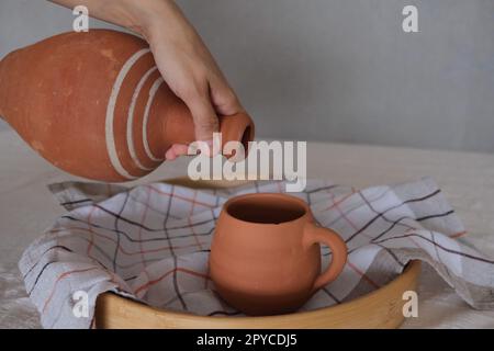 Vorderansicht eines alten unlackierten antiken Keramikkastens in einem Tablett auf einer traditionellen Tischdecke. Tonkrug und Becher zum Trinken von Wein oder Wasser. Stockfoto