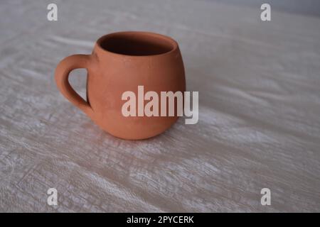 Vorderansicht einer alten, unlackierten antiken Keramikbecher auf einer Tischdecke. Tonbecher zum Trinken für Wein oder Wasser. Stockfoto