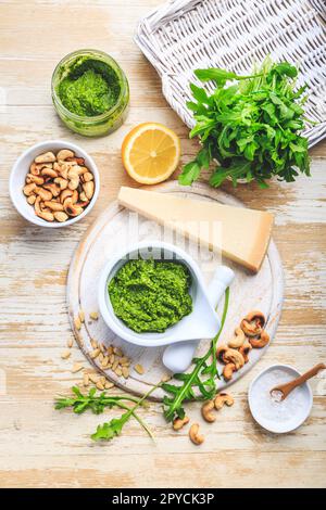 Hausgemachtes Rucola-Pesto mit Zutaten auf Holzhintergrund Stockfoto