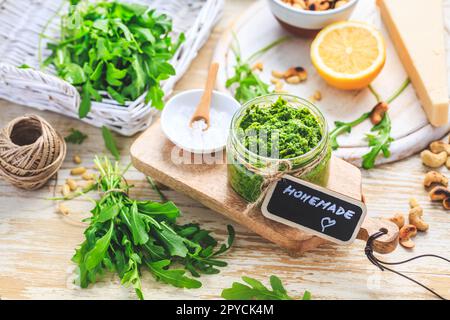 Hausgemachtes Rucola-Pesto mit Zutaten auf Holzhintergrund Stockfoto