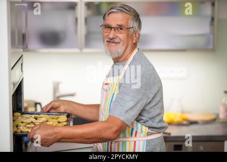 Ein älterer Mann bereitet gesundes Gemüse im Ofen zu und kocht sich für seine Familie Stockfoto