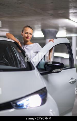 Tiefgarage (flaches, farbiges Bild des DOF) - eine junge Frau mit ihrem Auto in der Tiefgarage Stockfoto