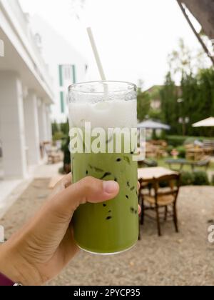 Halten Sie ein Glas Eistee mit Matcha-Grün in der Hand Stockfoto