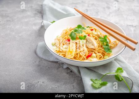 Gebratene Nudeln mit Hähnchen und Gemüse in eine weiße Schüssel rühren Stockfoto