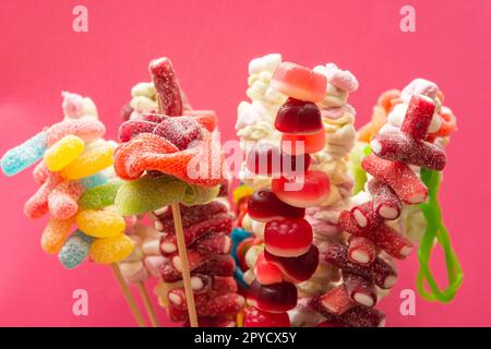 Variation bunter Fruchtgummi Süßigkeiten spießen saure Gummibären auf Holzspießen auf magentarotem Hintergrund Stockfoto