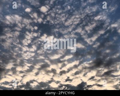 Wolken am Abendhimmel. Die Sonnenstrahlen durchdringen die Wolken. Blaue, gelbe und orangefarbene Farben des Himmels und der Wolken. Wunderschöne Landschaft. Die Sonne geht unter Stockfoto