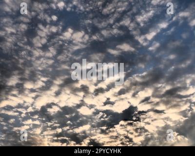 Wolken am Abendhimmel. Die Sonnenstrahlen durchdringen die Wolken. Blaue, gelbe und orangefarbene Farben des Himmels und der Wolken. Wunderschöne Landschaft. Die Sonne geht unter Stockfoto