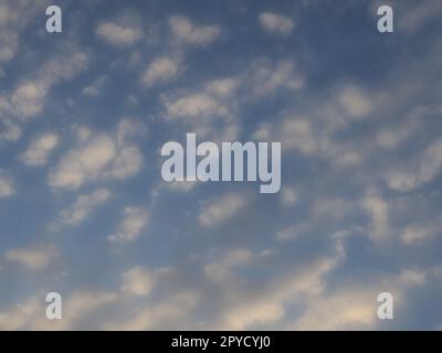 Wolken am Abendhimmel. Die Sonnenstrahlen durchdringen die Wolken. Blaue, gelbe und orangefarbene Farben des Himmels und der Wolken. Wunderschöne Landschaft. Die Sonne geht unter Stockfoto