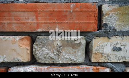 Backsteinmauer. Keramikmauerwerk oder Zaun. Alte, unebene Ziegel, an manchen Stellen mit Moos und Schimmel bedeckt. Die Textur des Steins oder Minerals. Der Einfluss von Feuchtigkeit auf Ziegelstrukturen. Dorfmotive Stockfoto