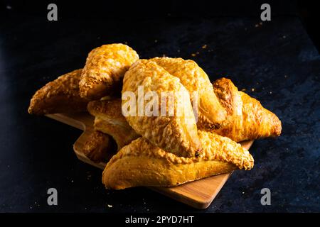 Frische französische Croissants, die in den Sonnenstrahlen glänzen, dunkler Hintergrund, Küche Stockfoto