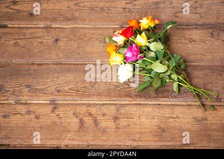 Farbenfrohe Rosenblüten auf altbraunem Holzhintergrund. Draufsicht mit Kopierbereich. Grußkarte für Mütter oder Frauen. Hochwertiges Foto. Stockfoto