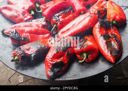 Rösten Sie köstliche rote Paprika für einen rauchigen Geschmack und schnelles Schälen. Balkansalatrezepte. Thermische Verarbeitung der Pfefferpflanze auf einem Metallkreis. Die Paprika werden auf einem flachen Backblech aufgemacht Stockfoto