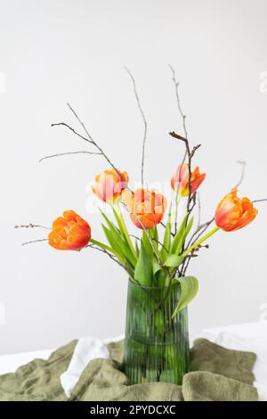 Ein sehr schöner Frühlingsstrauß in einer grünen Vase steht auf einem Tisch auf einer Tischdecke aus Leinen, orangefarbene Pfingstrosen. Muttertag, 8. März, Valentinstag. Stockfoto