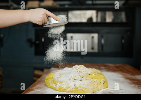 Die Bäckerhände streuen Mehl auf rohen Teig für Brot Stockfoto