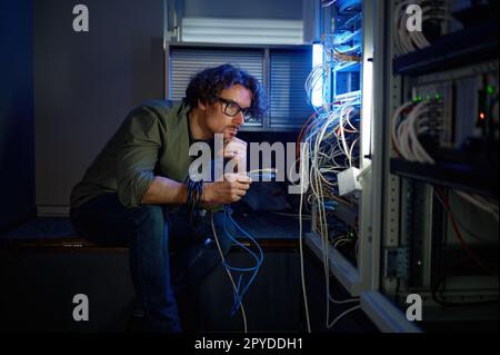 Männlicher Netzwerktechniker, der die Kabel im Serverraum anschließt Stockfoto