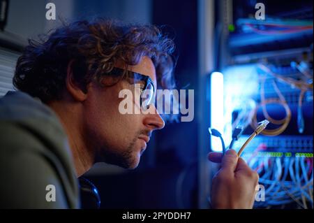 Nahaufnahme eines männlichen Netzwerkingenieurs, der die Kabel im Serverraum anschließt Stockfoto