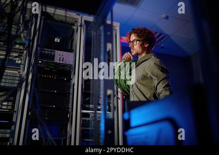 Rechenzentrumsingenieur mit vielen optischen Kabeln, die neben Computer-Racks laufen Stockfoto
