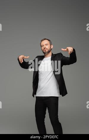Selbstbewusster Geschäftsmann im Anzug, der mit den Fingern auf die Kamera zeigt, isoliert auf grauem Stockbild Stockfoto